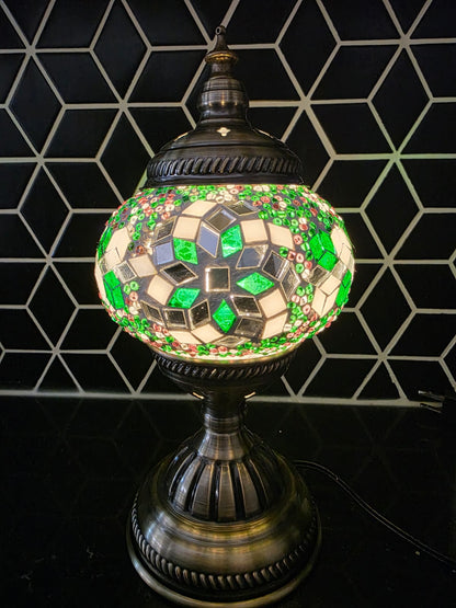 Decorative mosaic lamp with green and silver design against a geometric black and white tiled wall.