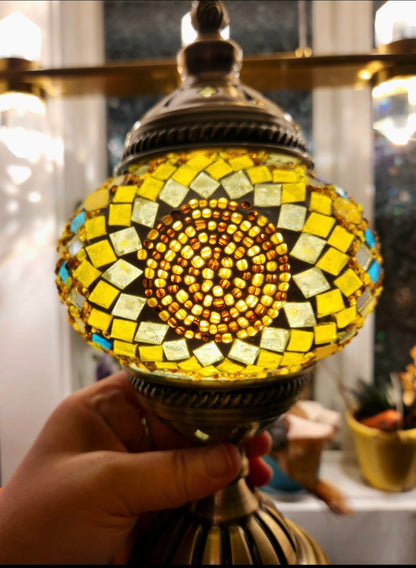 Decorative lamp with mosaic design held by a hand, blurred indoor background